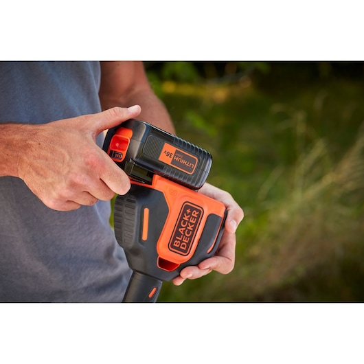 Photo of BLACK+DECKER BCSTA536L1 power tool with person inserting 36V lithium battery outdoors.