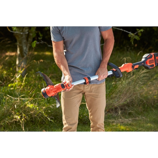BLACK+DECKER BCSTA536L1 grass trimmer in use outdoors, person adjusting the shaft length.