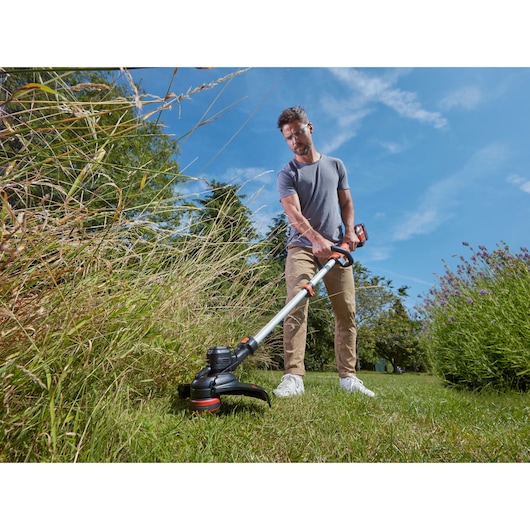 BLACKDECKER BCSTE636L1 cordless grass trimmer in use outdoors cutting tall grass, photography.