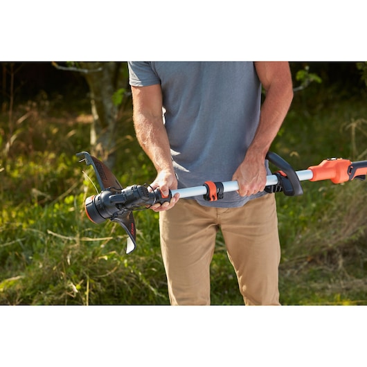 Photo of a person adjusting BLACK+DECKER BCSTE636L1 grass trimmer in outdoor setting.