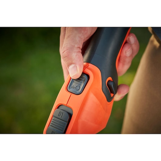 Close-up photo of a hand pressing the power button on a BLACKDECKER BCSTE636L1 orange and black garden tool.