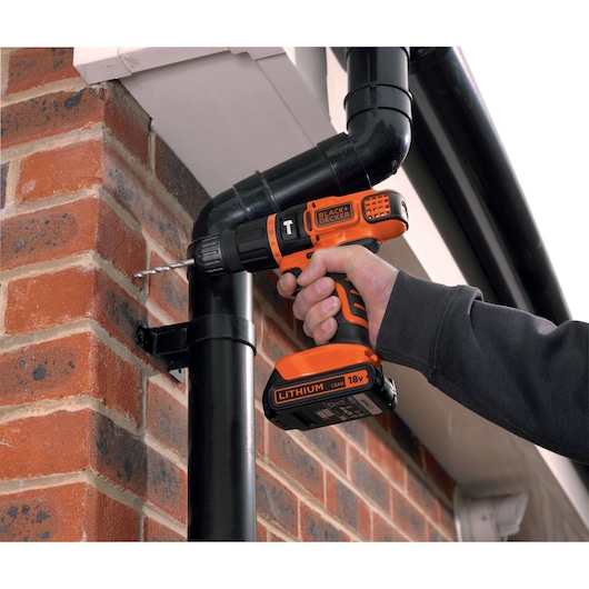 BLACKDECKER BDCH188N cordless drill in use drilling into brick wall near black pipe, close-up view.