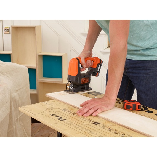 BLACK+DECKER BDCJS12N jigsaw in use cutting wood, shown in a workshop setting.