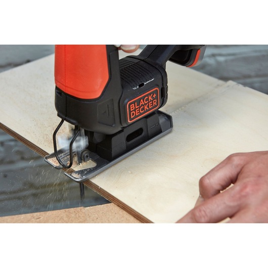 Photo of BLACK+DECKER BDCJS12N jigsaw cutting plywood, close-up on tool and user's hand.