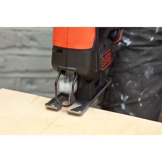 BLACKDECKER BDCJS12S1 jigsaw cutting wood, close-up of blade in motion next to wooden surface.