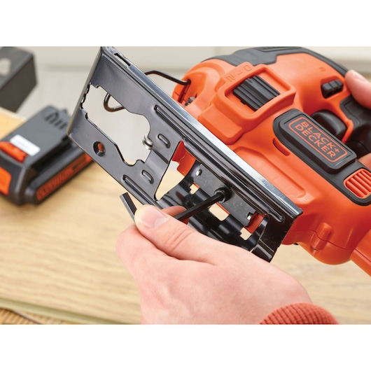 Photo of BLACK+DECKER BDCJS18M1 cordless jigsaw being adjusted with hex key, close-up on orange and black tool.