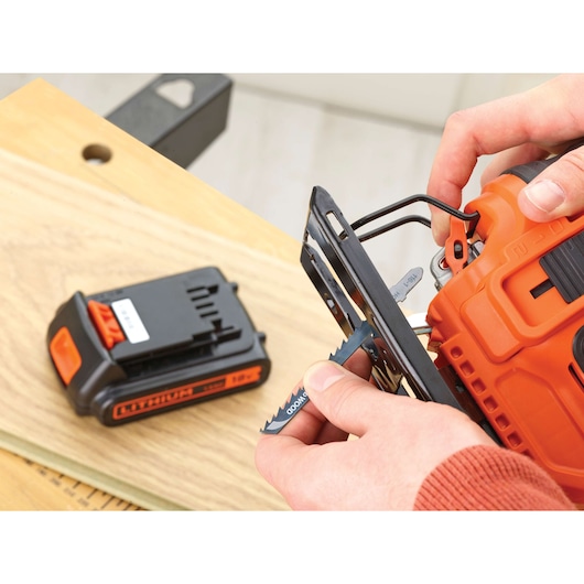 Photo of BLACKDECKER BDCJS18M1 cordless jigsaw with blade being inserted, battery pack on wooden surface.