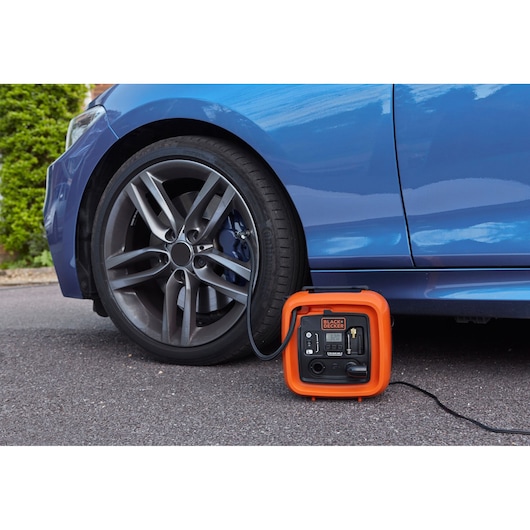 BLACKDECKER BDCOM400 portable air compressor inflating a car tire on asphalt.