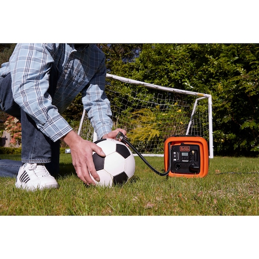 BLACKDECKER BDCOM400 portable air compressor inflating a soccer ball in a yard near a goal post.