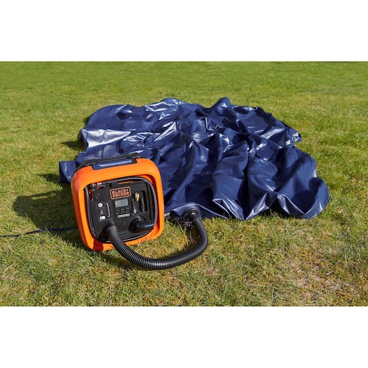 BLACKDECKER BDCOM400 orange air inflator with hose on grass beside deflated blue inflatable, outdoor view.