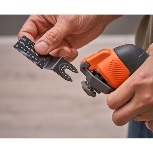 BLACKDECKER BDCOS18N oscillating tool held in hand with wood and metal blade being attached, close-up.