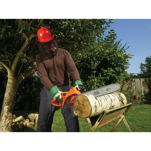 Person using BLACKDECKER BDCS20 chainsaw to cut log on stand outdoors, wearing safety gear.