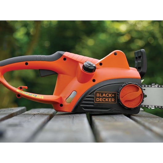 Photo of BLACK+DECKER BDCS20 orange and black chainsaw side view on wooden table outdoors.