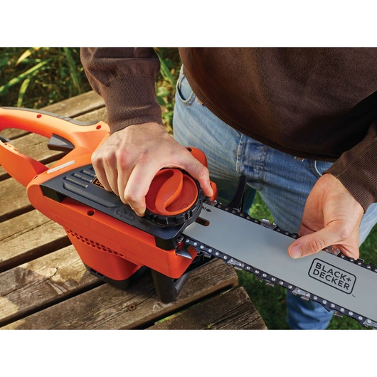 Photo of BLACK+DECKER BDCS20 chainsaw being adjusted by hand, close-up on orange and silver tool.