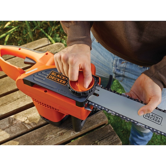 BLACK+DECKER BDCS20 chainsaw being adjusted, orange and black, close-up outdoors.