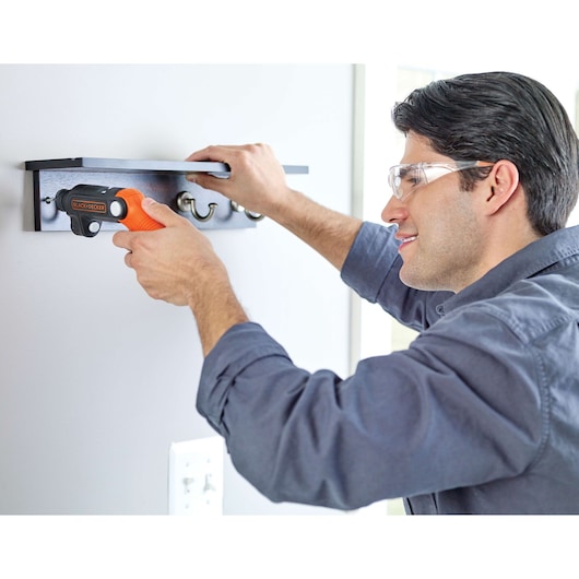 BLACK+DECKER BDCSFL20C cordless screwdriver in use mounting a wall hook rack indoors.