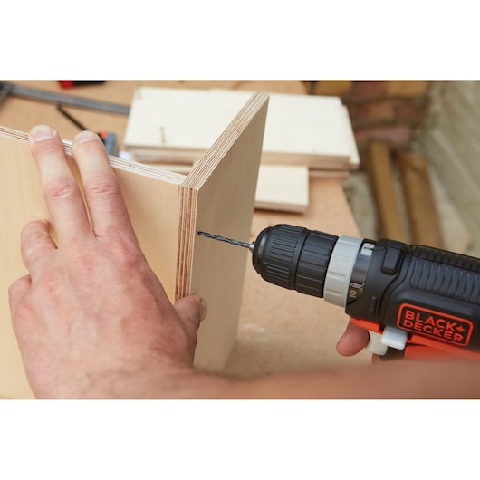 BLACK+DECKER BDDD12 cordless drill used to drill into plywood in a workshop setting.