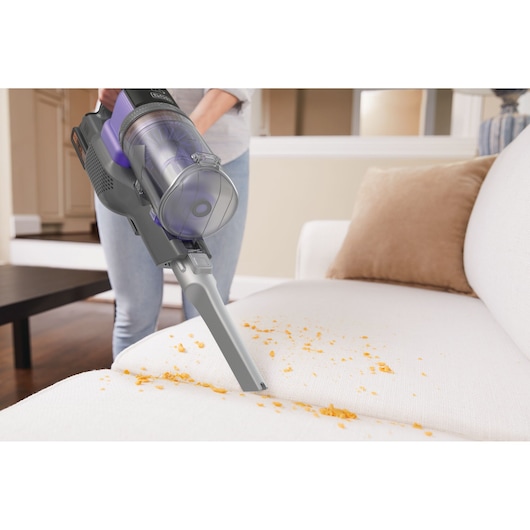 BLACKDECKER BDPSE1815P cordless vacuum cleaning crumbs from a white sofa in a living room, side view.