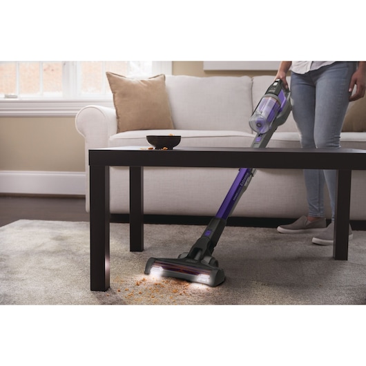 Photo of BLACKDECKER BDPSE1815P cordless stick vacuum cleaning crumbs under a coffee table in a living room.