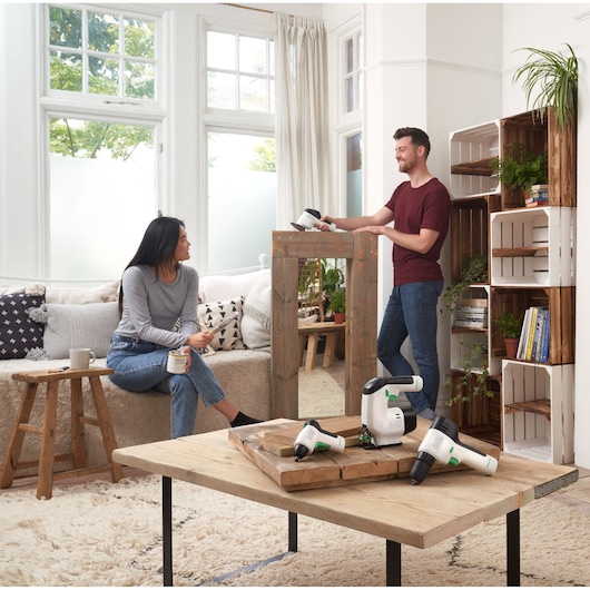 BLACKDECKER BDST60120 power tools on a wooden coffee table in a modern living room, two people in background.