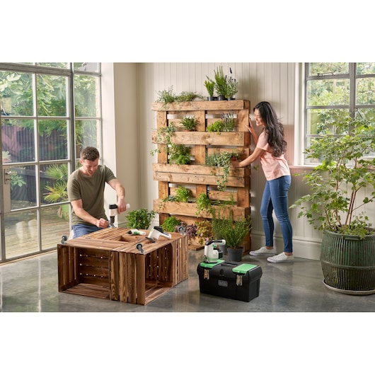 Photo of BLACKDECKER BDST60120 black toolbox with green latches on floor beside wooden planter and tools.