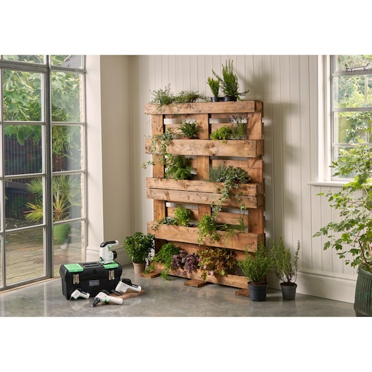 BLACKDECKER BDST60120 tool box and garden tools next to a wood pallet vertical herb garden indoors, side angle.