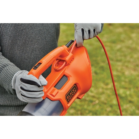 Photo of BLACKDECKER BEBL185 orange handheld leaf blower with cord held by gloved hands outdoors.