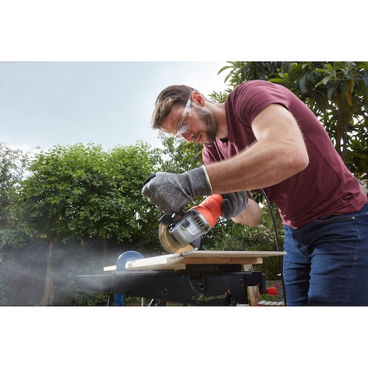 Photo of a person using a BLACKDECKER BEG010K circular saw to cut wood outdoors, wearing safety gloves.