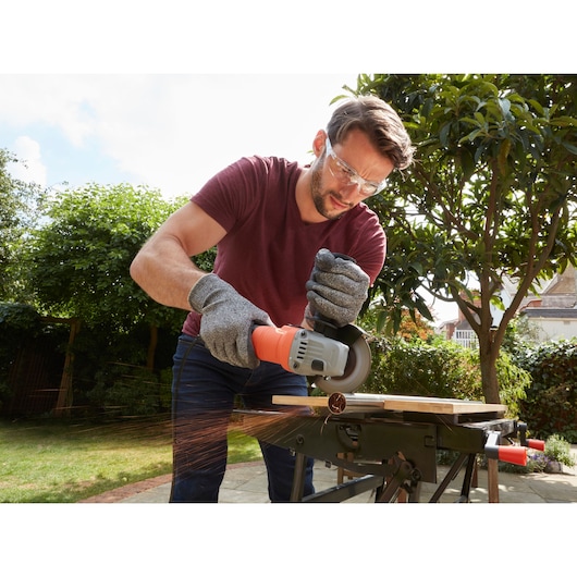 Photo of a person using BLACKDECKER BEG010K angle grinder on metal outdoors, sparks flying, work gloves worn.