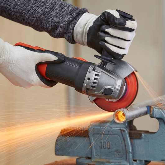 BLACKDECKER BEG210KA2 angle grinder in use, cutting metal pipe with sparks, close-up view of hands with gloves.