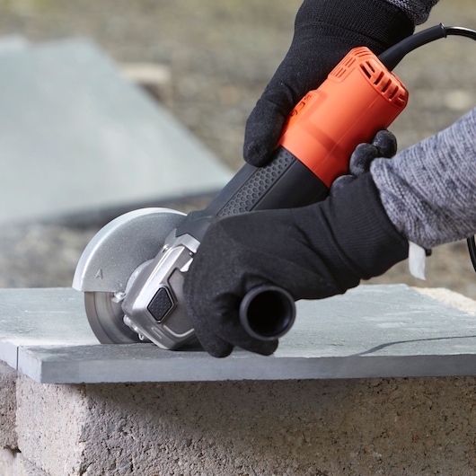 BLACKDECKER BEG210KA2 angle grinder in use, orange and black, cutting stone slab outdoors.