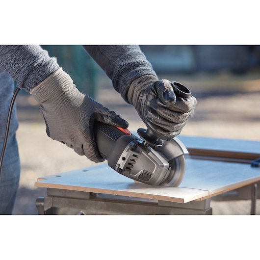 BLACKDECKER BEG210K angle grinder in use, cutting tile, close-up of hands wearing gloves.