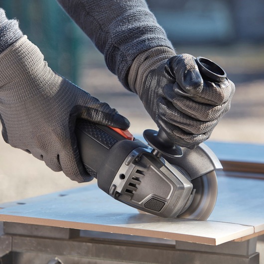 BLACKDECKER BEG220A6 angle grinder in use cutting a tile, close-up of gloved hands operating tool.