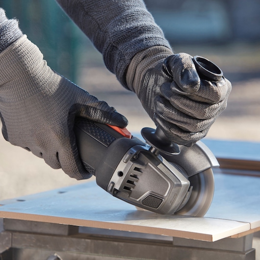 BLACKDECKER BEG220KA5 angle grinder cutting tile, close-up of gloved hands holding tool.