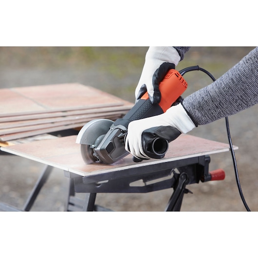 Photo of BLACKDECKER BEG220K angle grinder cutting a tile, operated by gloved hands outdoors.