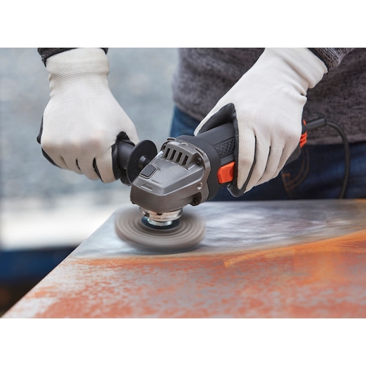 BLACKDECKER BEG220K angle grinder in use on metal surface, close-up with gloved hands.