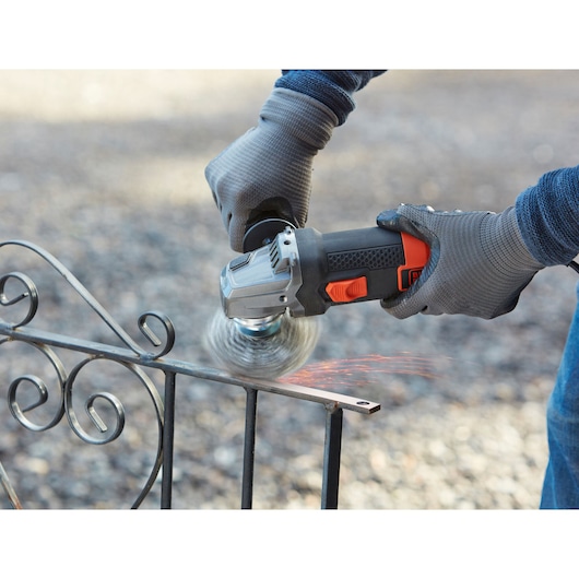 BLACK+DECKER BEG220 angle grinder in use on metal outdoor fence, close-up with gloves.