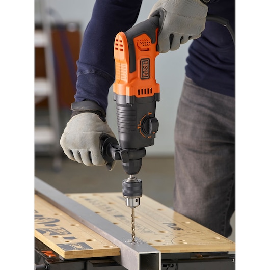 BLACKDECKER BEHS01K corded hammer drill in use, drilling metal on workbench, ergonomic handle visible.