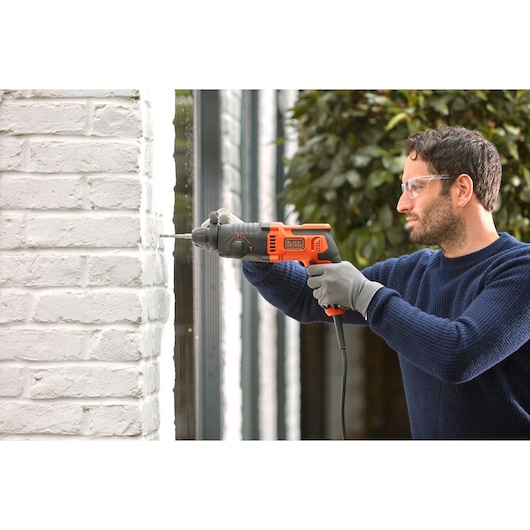 BLACKDECKER BEHS01K corded hammer drill used on white brick wall, orange and black design, side view.