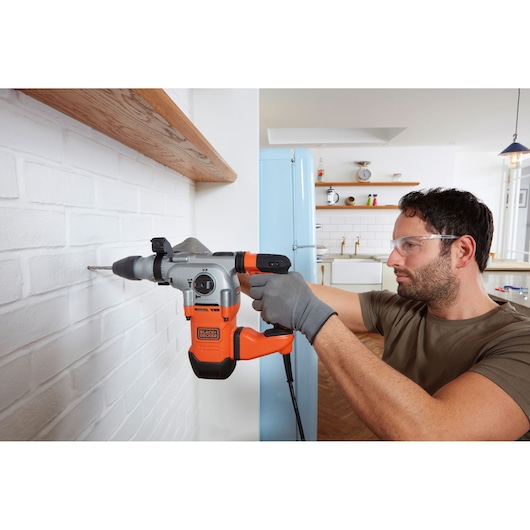 Photo of BLACKDECKER BEHS03K rotary hammer drill in use drilling into a white brick wall.