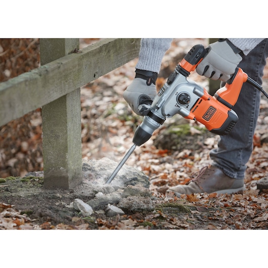 BLACK+DECKER BEHS03K rotary hammer drill used outdoors on concrete near a wooden fence.