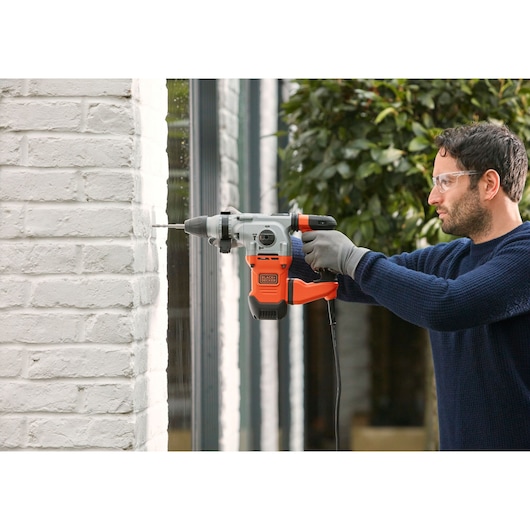 BLACKDECKER BEHS03K corded hammer drill used on white brick wall, orange and black accents, outdoor setting.