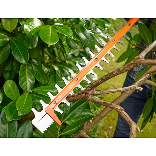 BLACKDECKER BEHTS301 hedge trimmer blade cutting a thick tree branch, close-up in garden setting.