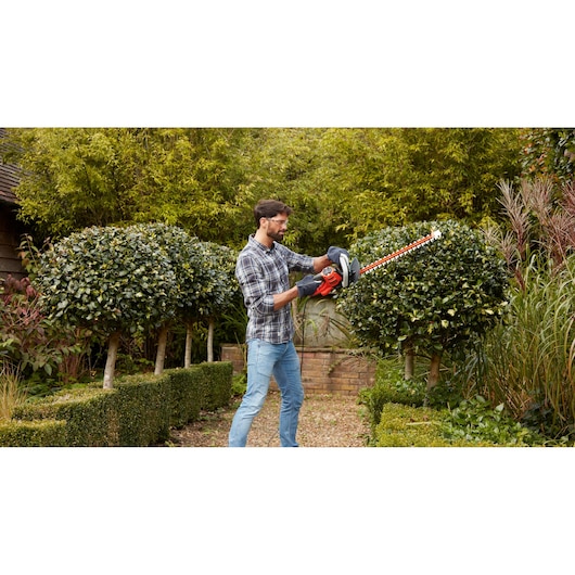 Person using BLACK+DECKER BEHTS455 hedge trimmer to trim bushes in a garden.