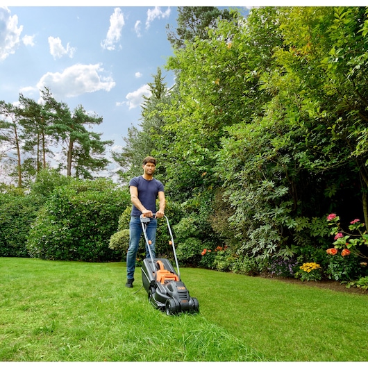 BLACKDECKER BEMW351 lawn mower used outdoors on grass, garden background, side angle.