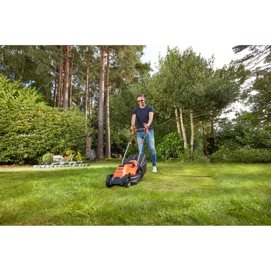 BLACKDECKER BEMW451BH electric lawn mower in use outdoors on grass lawn, garden setting.