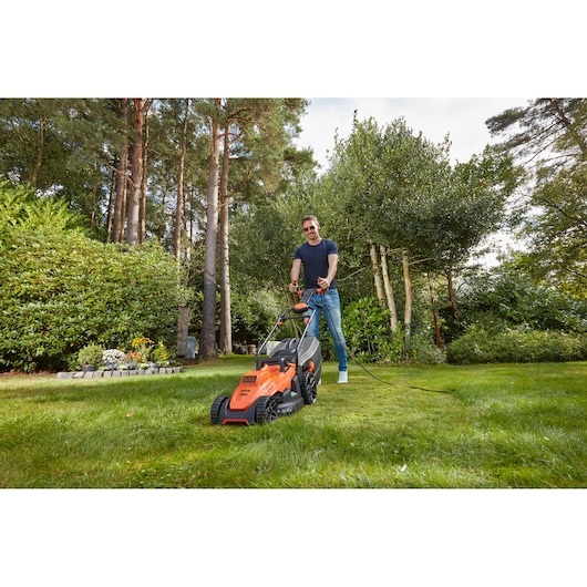 Photo of BLACKDECKER BEMW461ES electric lawn mower in use on a grassy lawn, orange color, garden background.