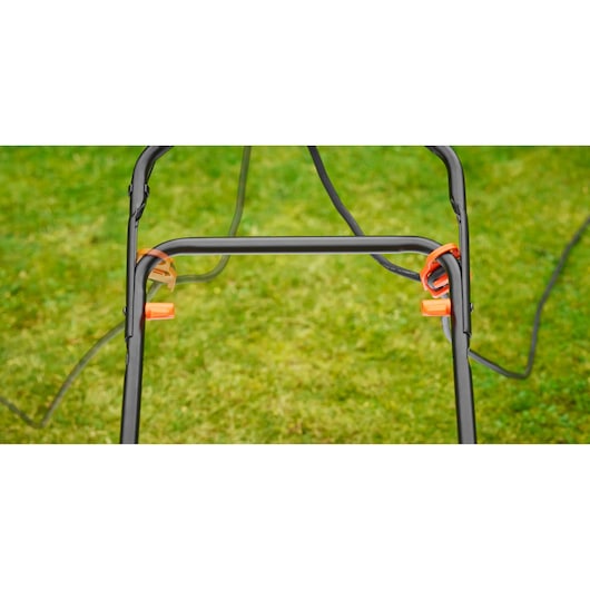 Close-up of BLACK+DECKER BEMW461ES lawn mower handle with orange cable clips outdoors on grass.