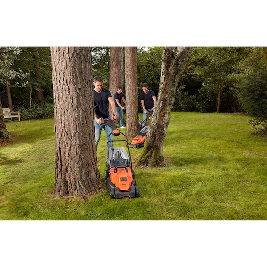 BLACKDECKER BEMW461ES lawn mower used by people mowing grass around trees in a garden.