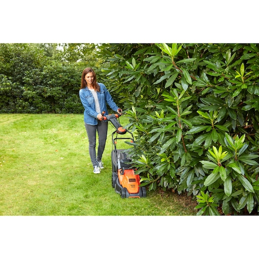 BLACKDECKER BEMW471ES lawn mower in use on grass near bushes outdoors.